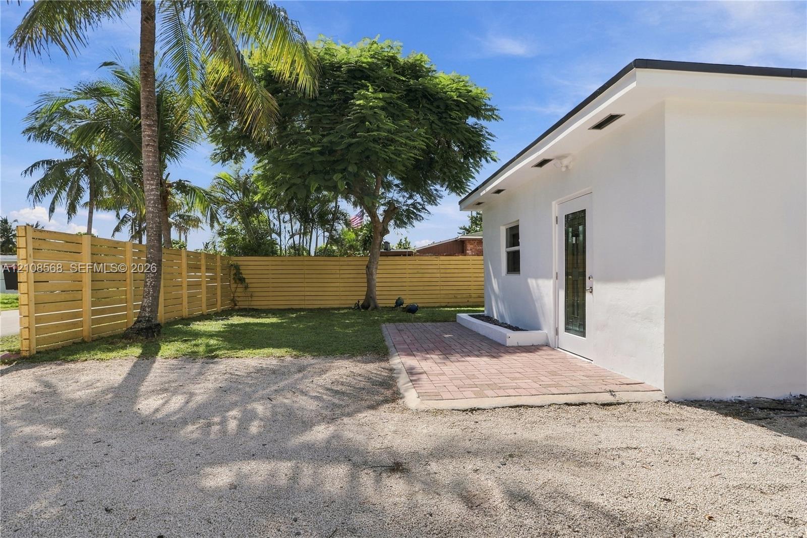 Exterior grounds featuring a paved brick patio, light-toned gravel area, horizontal wood-slat fencing, and established palm trees