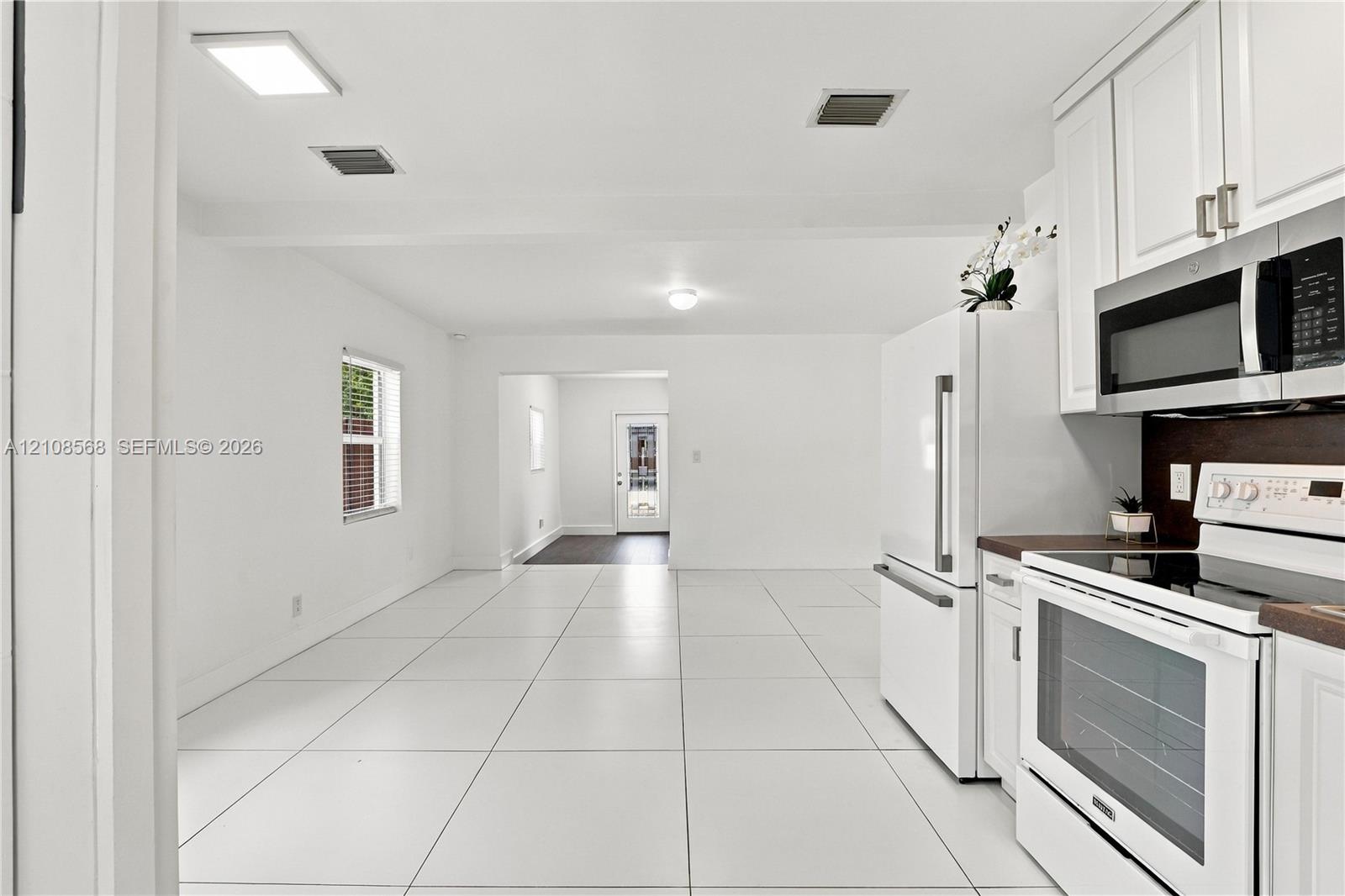 Kitchen featuring white cabinetry, solid-surface countertops, white appliances, and large-format tile flooring