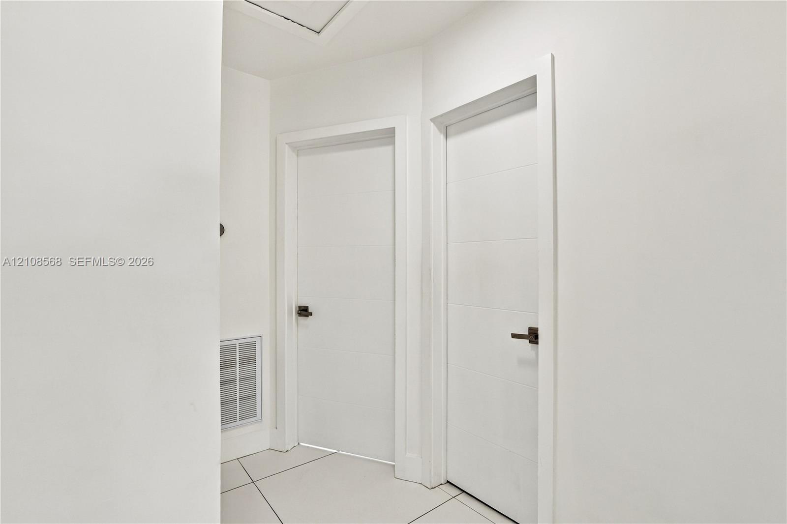 Neutral interior hallway featuring large-format tile flooring and minimalist flat-panel doors with matte black hardware