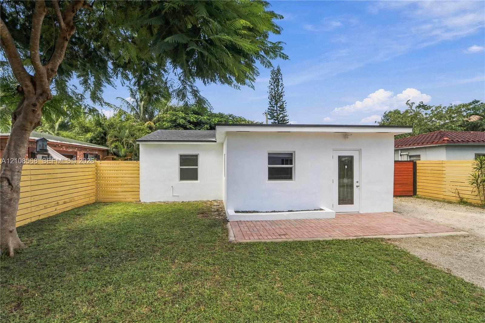 Exterior featuring white stucco siding, a brick paver patio, wood horizontal slat fencing, and a manicured lawn