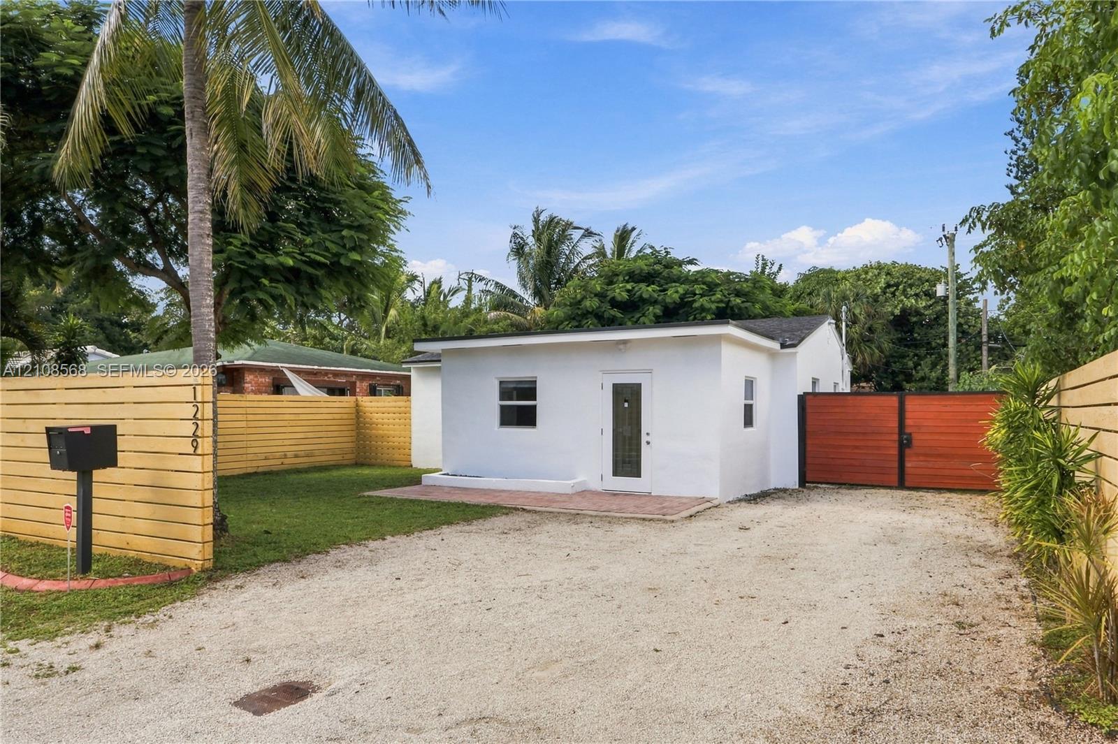 Exterior facade featuring white stucco finish, a paved front patio, horizontal wood privacy fencing, and a gated side entrance