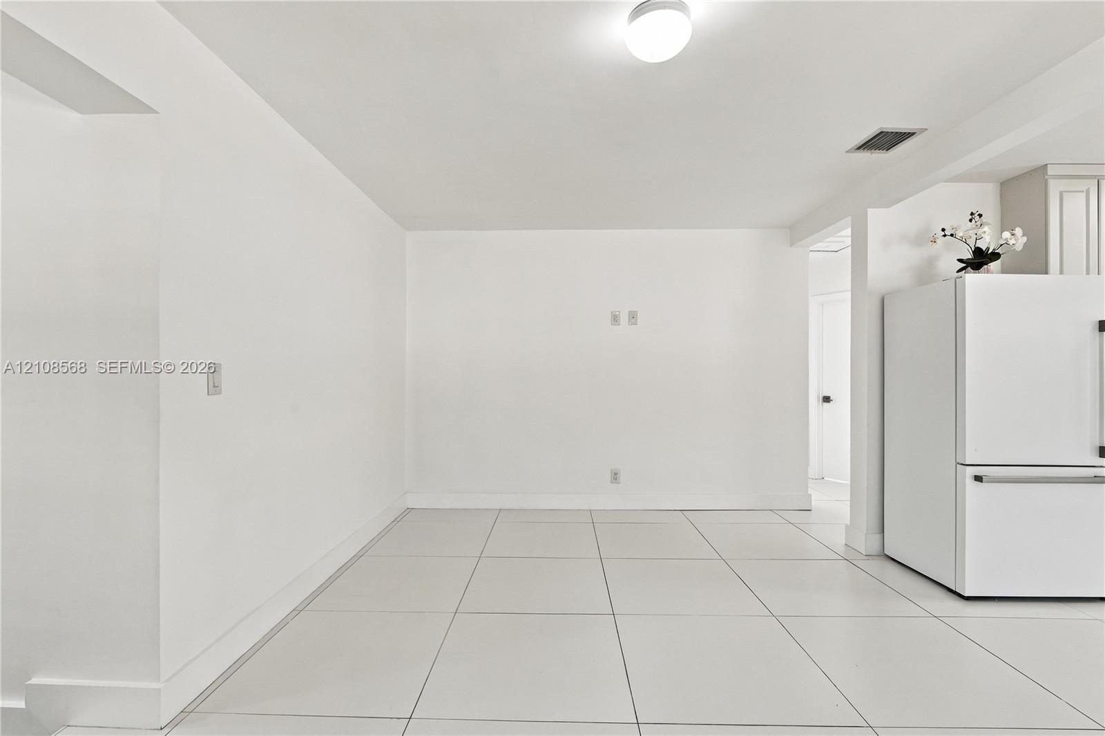 Neutral-toned interior space featuring large-format ceramic tile flooring, bright white wall finishes, and a built-in stainless steel refrigerator