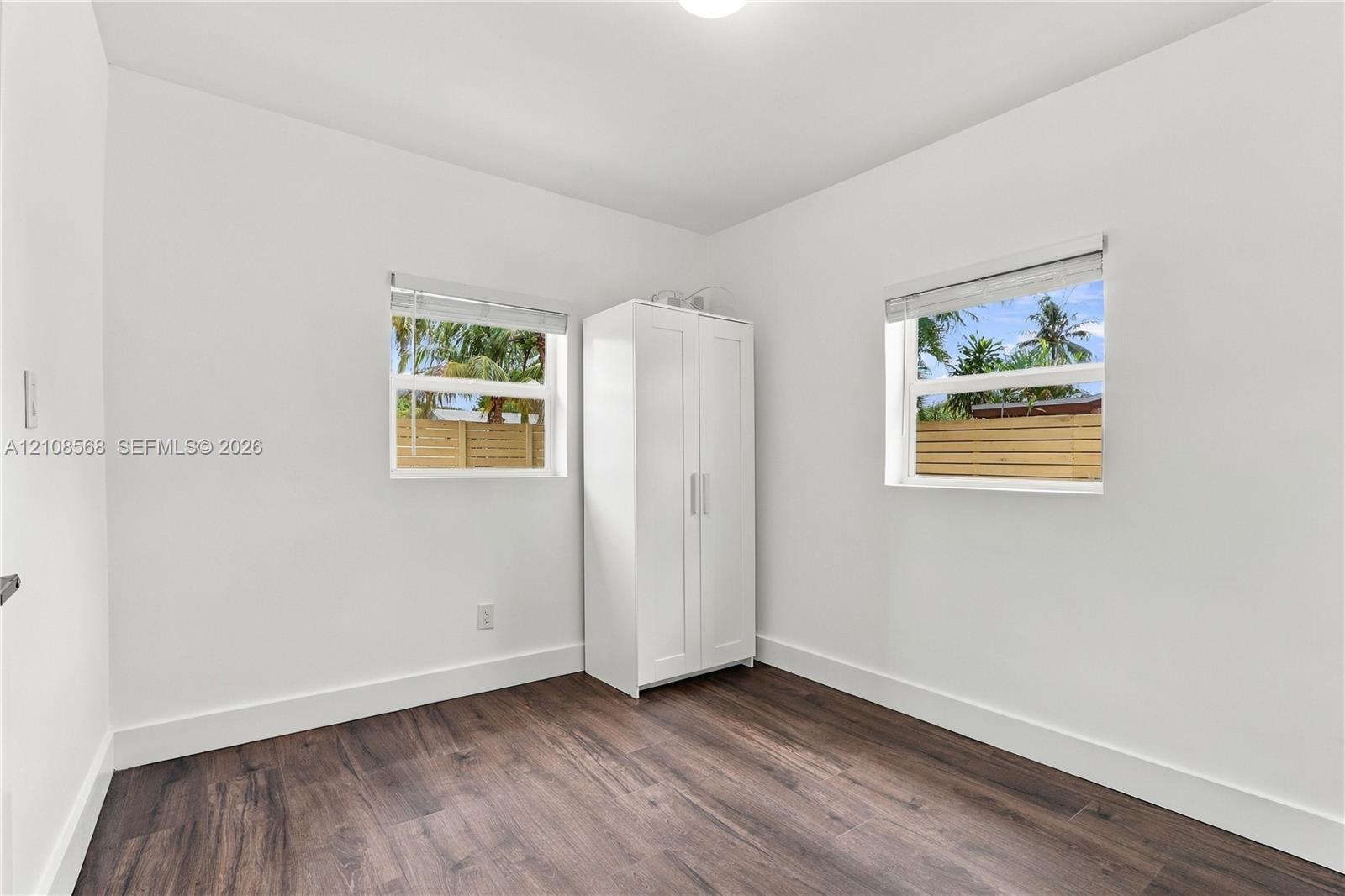 Neutral-toned interior room featuring wood-finish flooring, two dual-pane windows with horizontal blinds, and a white ceiling-mounted light fixture