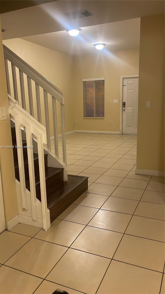 Entryway featuring large-format tile flooring, staircase with dark wood-finish treads and white balusters, and flush-mount ceiling lighting