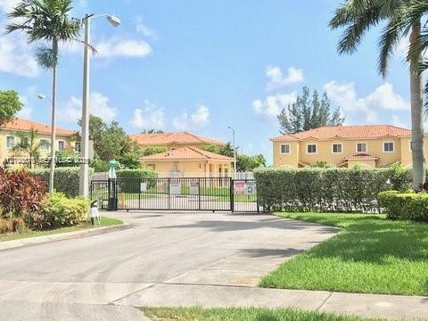 Gated entrance featuring a metal security gate, concrete driveway, and mature perimeter landscaping Gated entrance featuring a metal security gate, concrete driveway, and mature perimeter landscaping