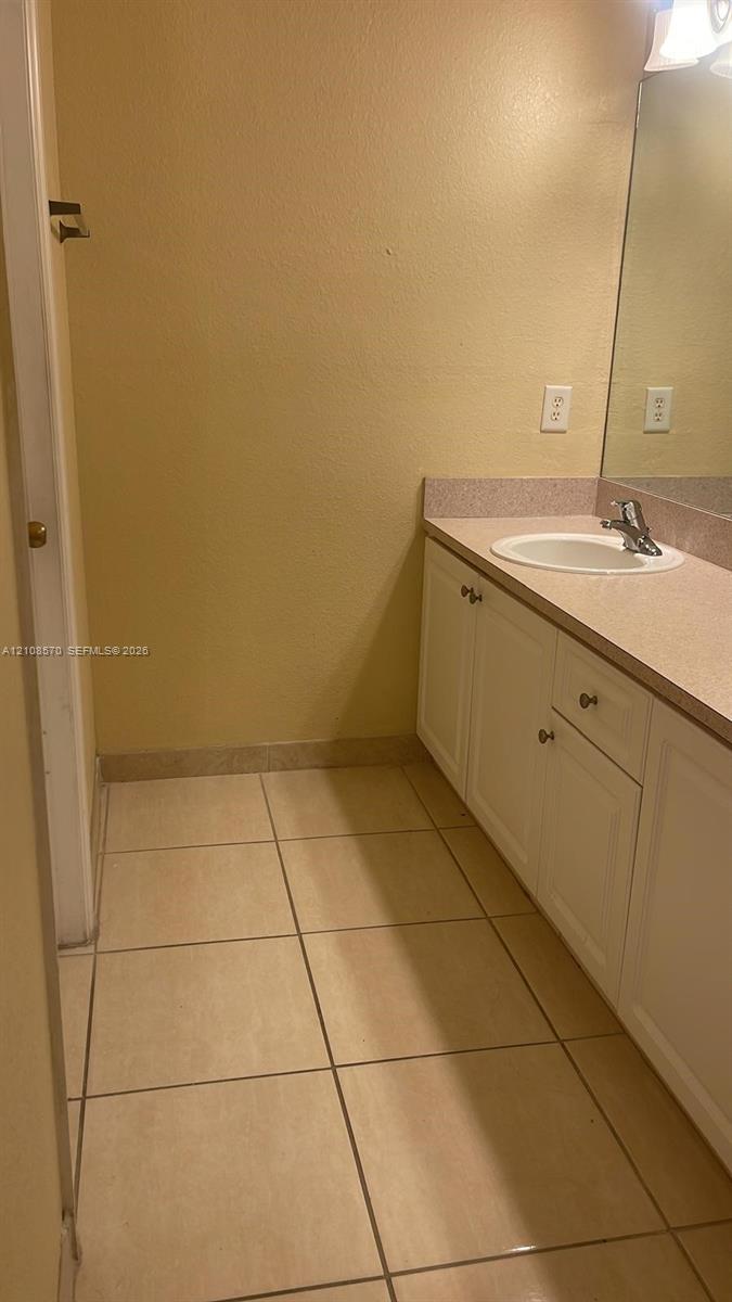 Bathroom vanity featuring white cabinetry, a solid-surface countertop, an integrated sink, and tile flooring