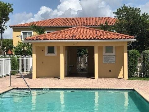 Swimming pool with a metal handrail and paved deck, featuring a covered pavilion with a terracotta tile roof