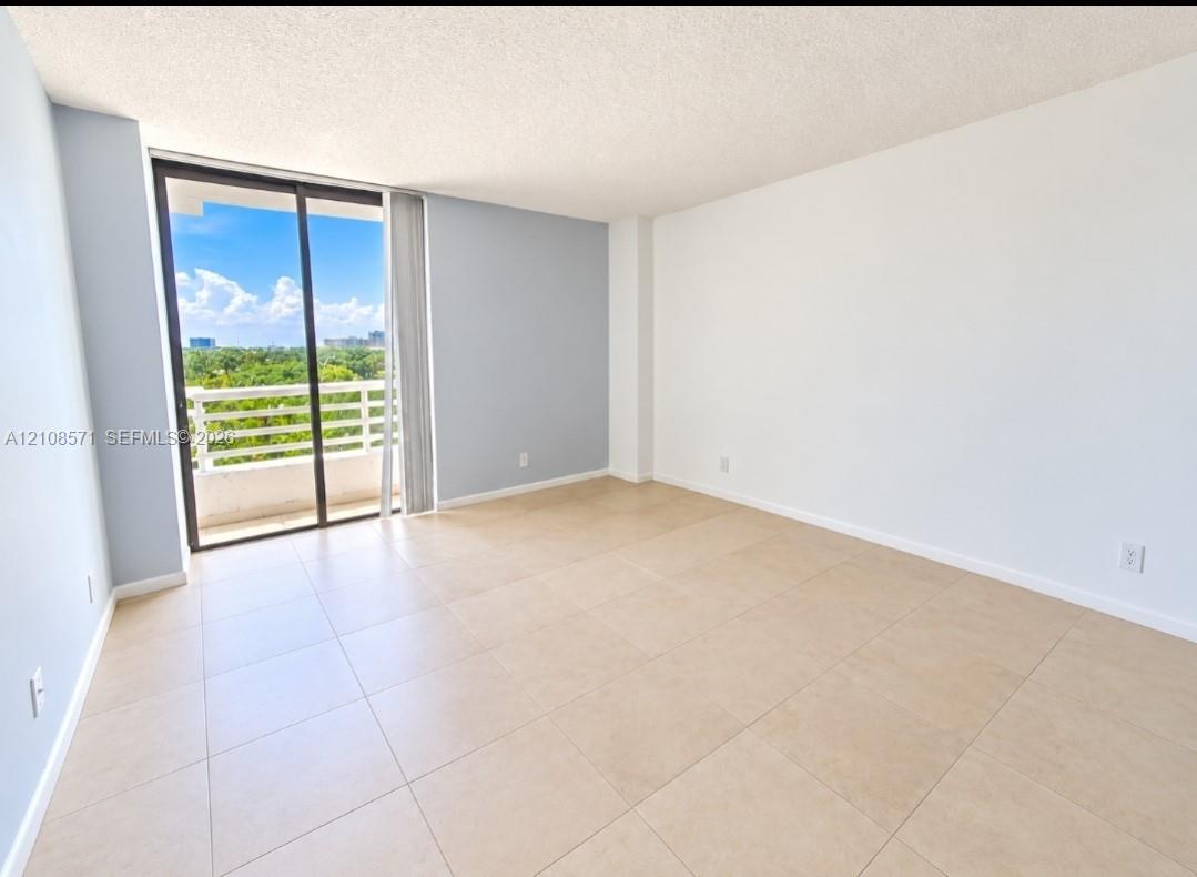 Neutral-toned tile flooring, light-colored walls, and floor-to-ceiling sliding glass doors opening to a private balcony