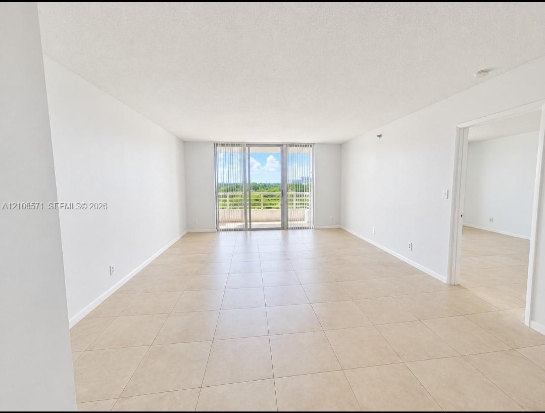 Neutral interior featuring light-toned tile flooring, floor-to-ceiling glass sliding doors, and a private balcony