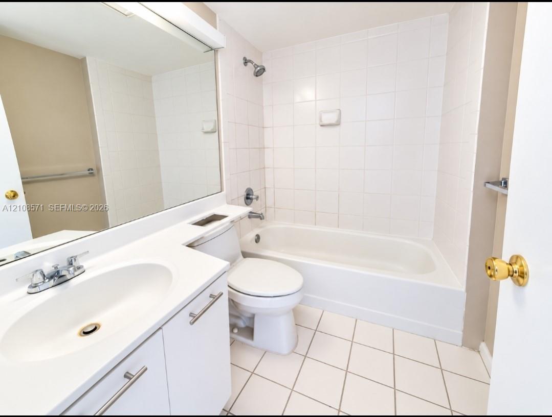 Bathroom featuring a white vanity with an integrated basin, wall-to-wall mirror, tiled shower and tub enclosure, and ceramic tile flooring