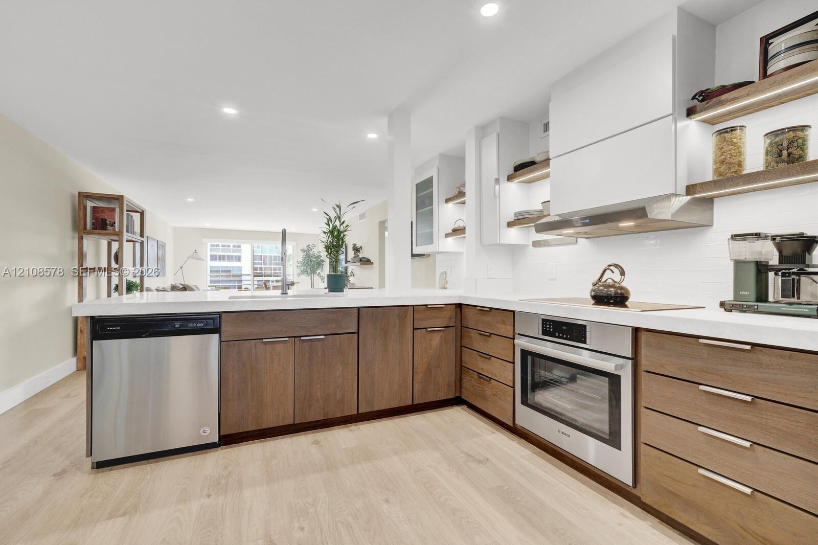 Kitchen featuring flat-panel wood-finish cabinetry, white countertops, stainless steel appliances, open shelving with integrated lighting, and wood-finish flooring