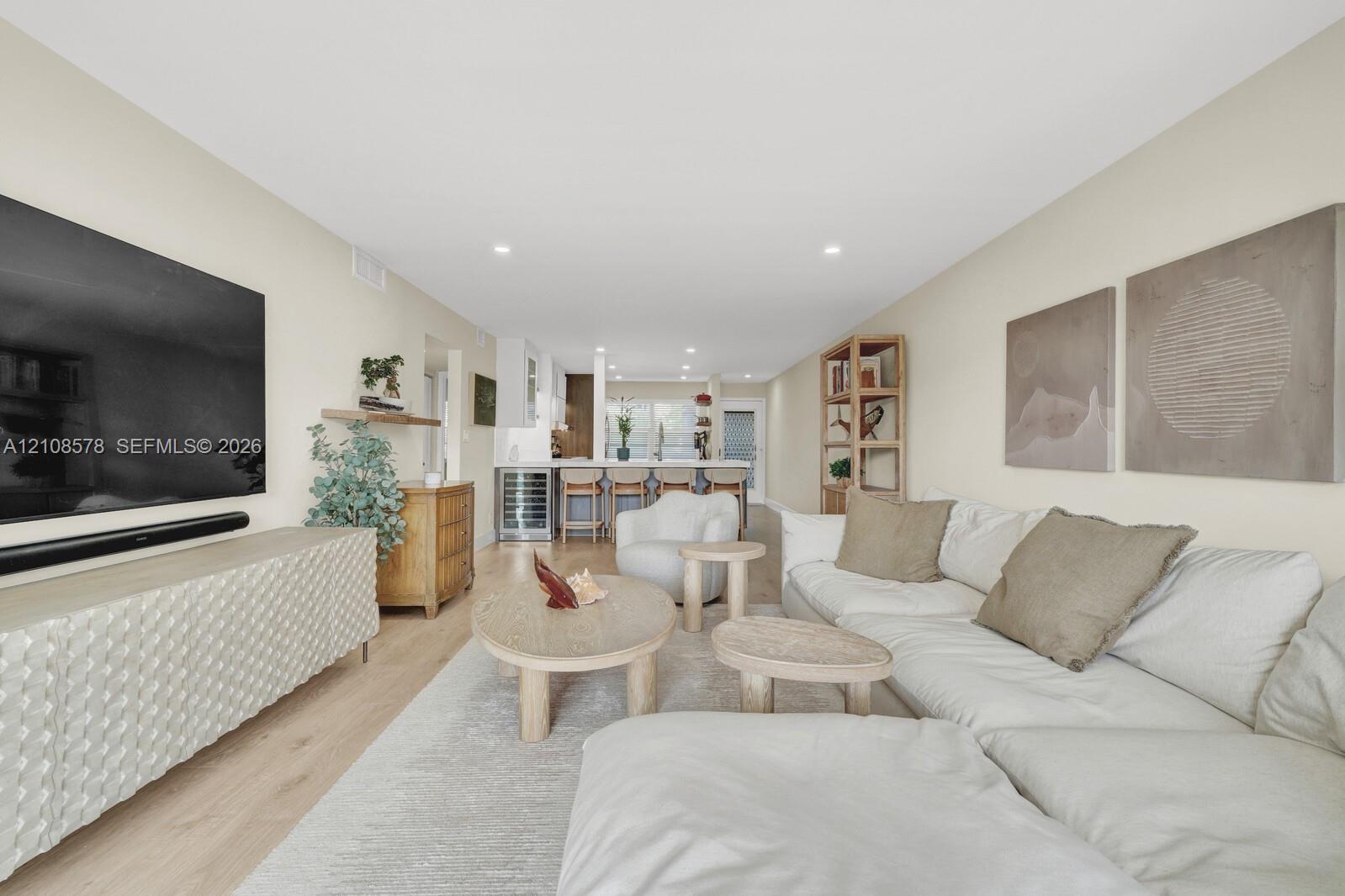 Open-concept interior featuring light wood-finish flooring, recessed lighting, and a kitchen equipped with a built-in wine refrigerator and a breakfast bar