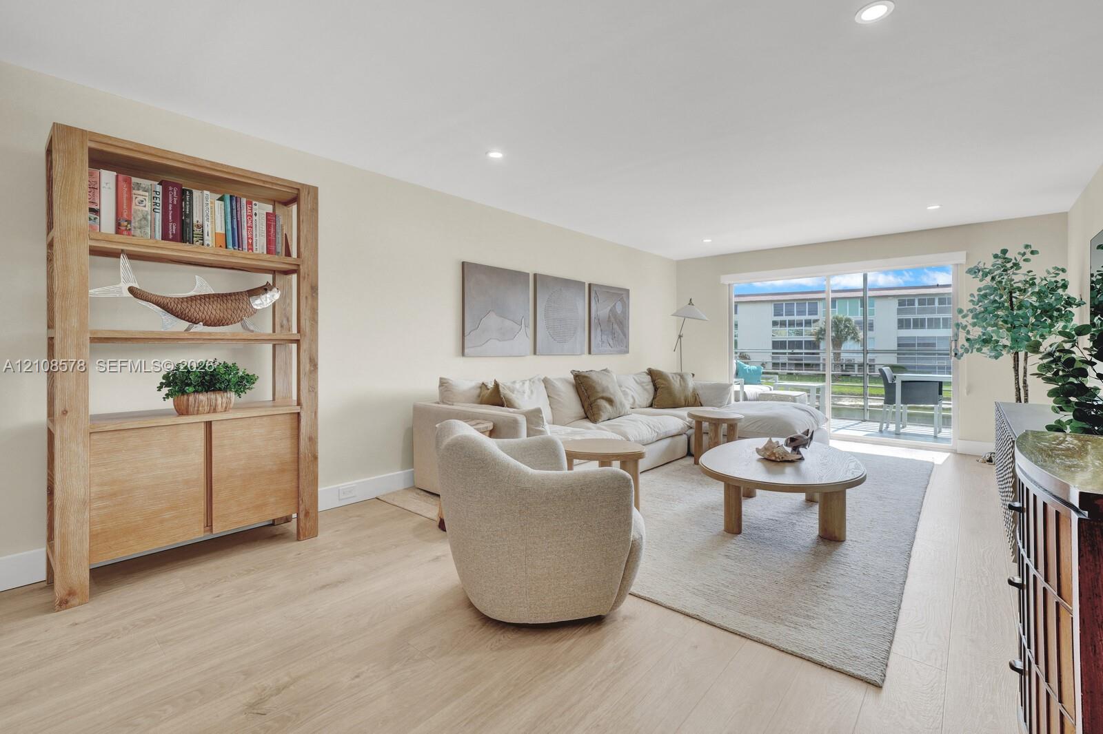 Living area featuring light-toned wood-finish flooring, recessed lighting, and large sliding glass doors leading to an exterior screened balcony