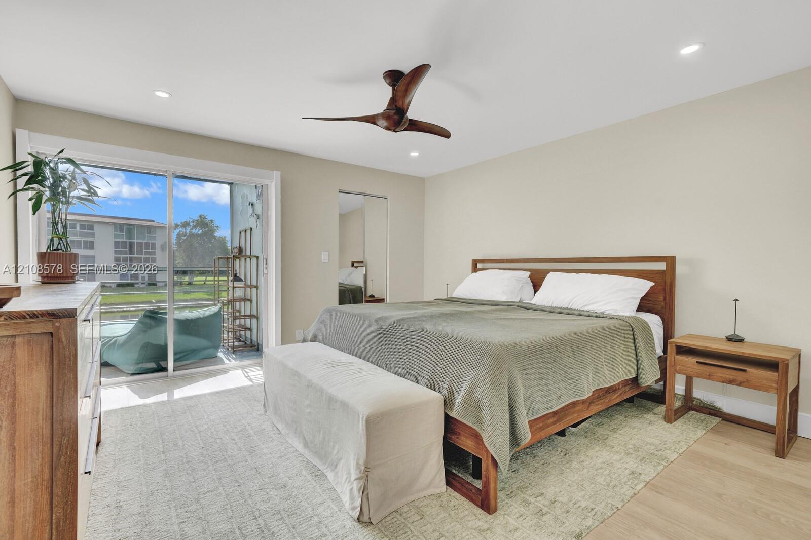 Sliding glass door access to a private balcony, wood-finish flooring, recessed lighting, and a multi-blade ceiling fan
