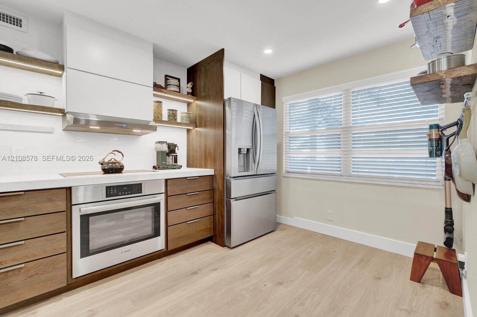 Kitchen featuring wood-finish cabinetry, white slab countertops, stainless steel appliances, open wood shelving, and wood-finish tile flooring