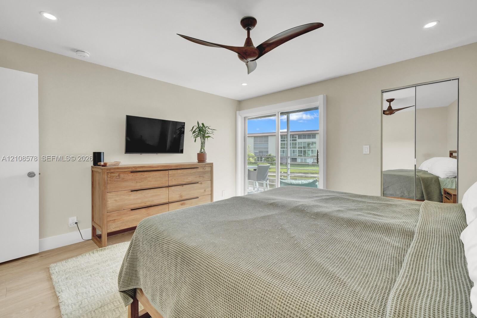 Room featuring recessed lighting, a multi-blade ceiling fan, wood-finish flooring, sliding glass door access to the exterior, and a closet with mirrored sliding doors
