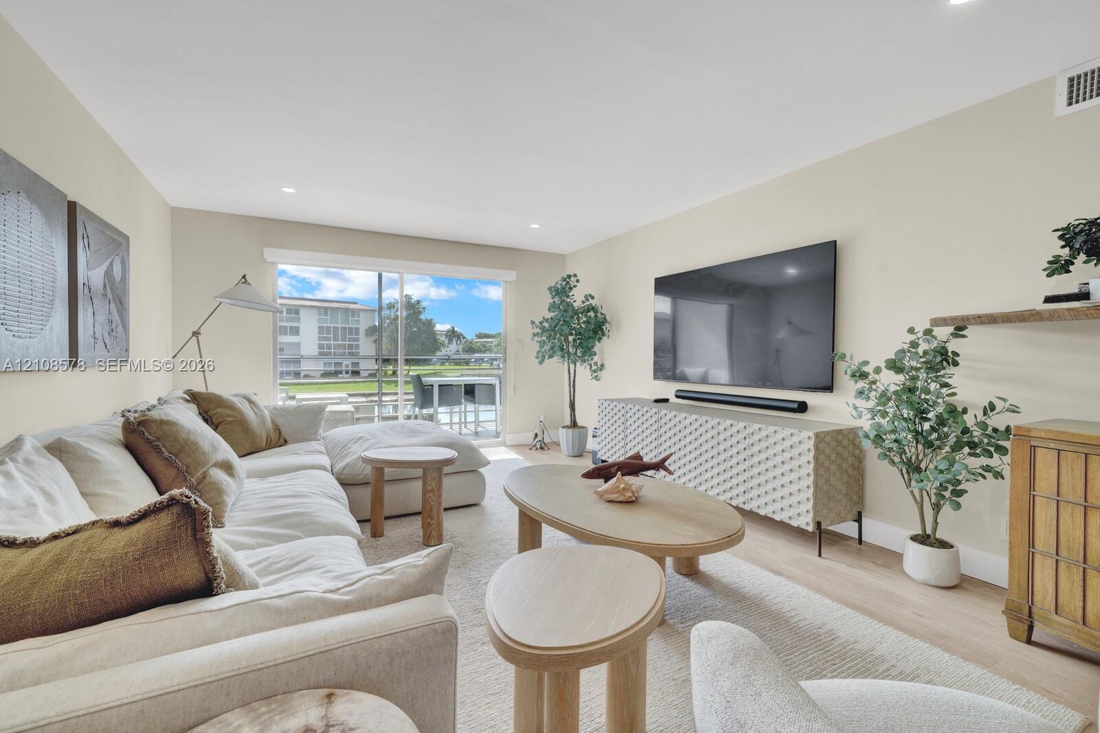 Living area featuring light-toned wood-finish flooring, recessed lighting, and large sliding glass doors providing outdoor access