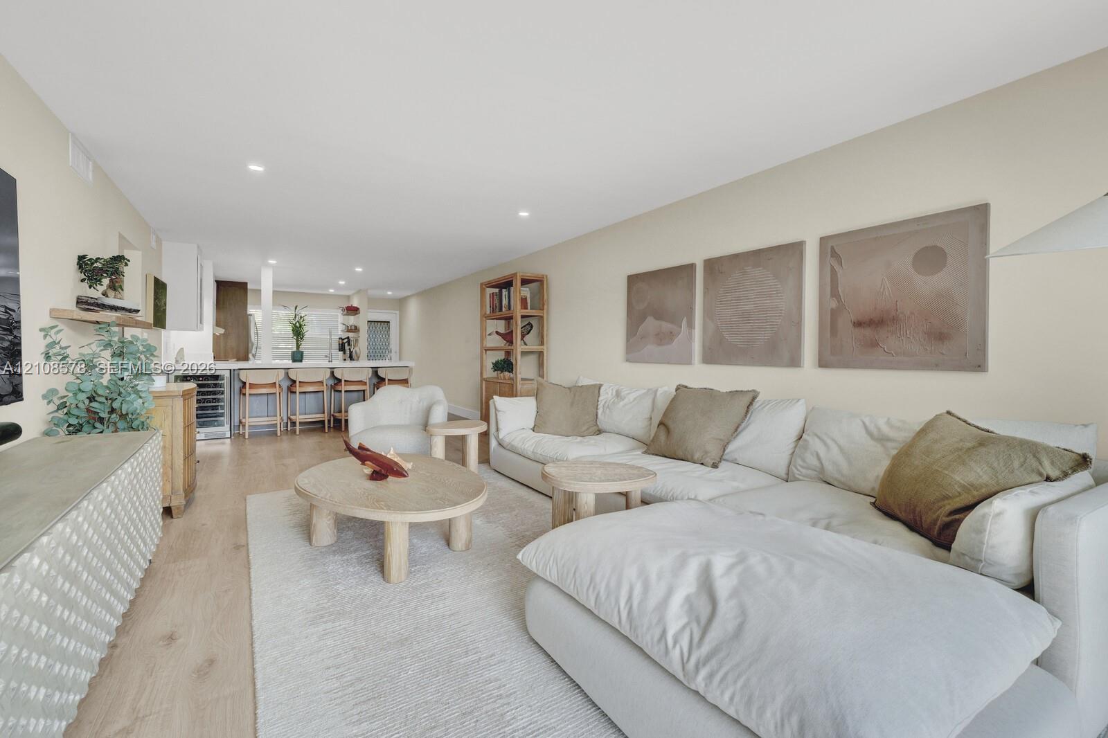 Open-concept interior featuring light wood-finish flooring, recessed lighting, and a breakfast bar equipped with a built-in beverage refrigerator