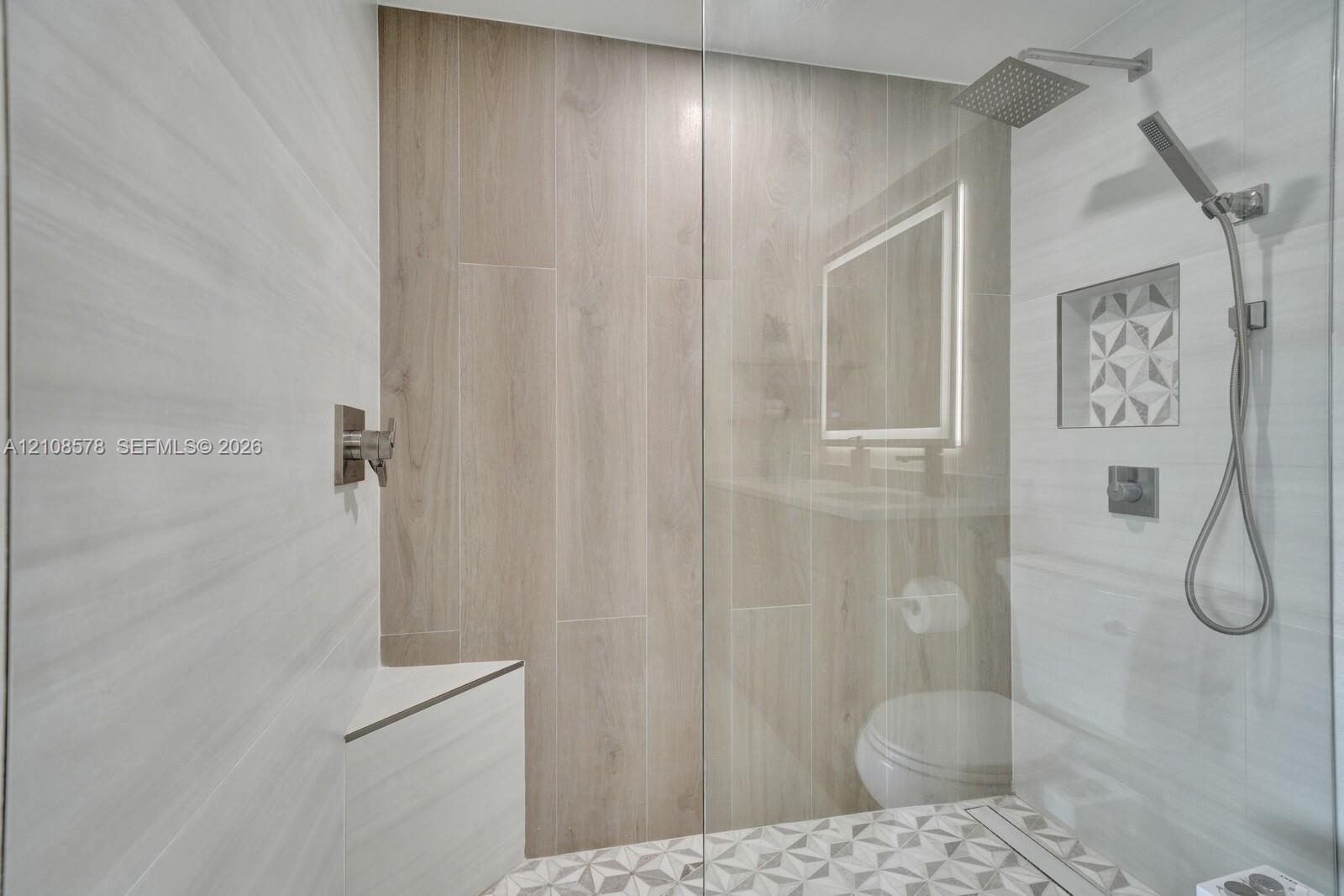 Walk-in shower featuring wood-finish tile surround, a built-in corner bench, a rainfall showerhead with a handheld sprayer, and a decorative tile-lined wall niche