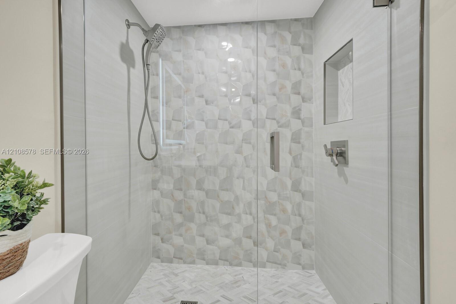 Walk-in shower featuring a frameless glass door, geometric patterned accent tile, built-in wall niche, herringbone floor tile, and multi-setting handheld shower head