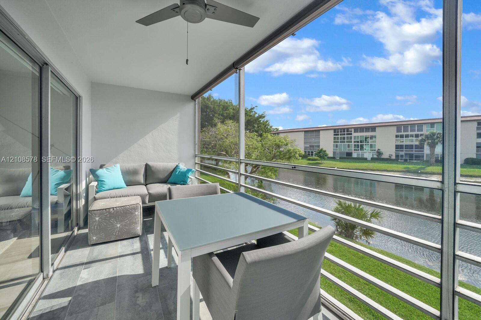 Screened-in balcony featuring grey tile flooring, a ceiling fan, and metal railings overlooking a canal