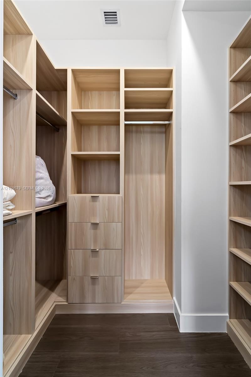 Custom wood-finish storage system featuring floor-to-ceiling shelving, integrated garment rods, four built-in drawers with metallic pulls, and dark wood-finish flooring