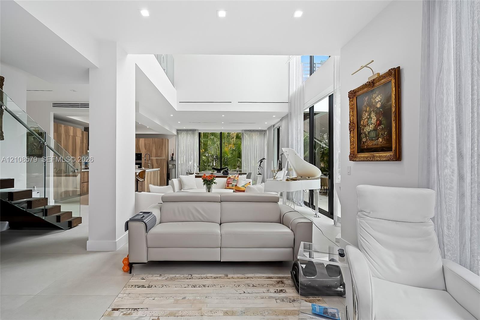 Double-height ceiling, open-concept floor plan, recessed lighting, staircase with glass railings, and floor-to-ceiling windows