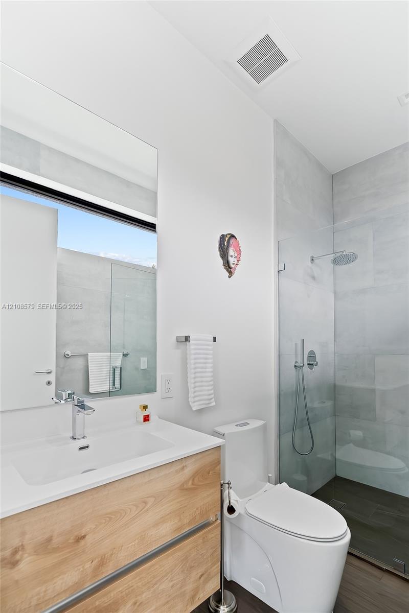 Modern vanity with wood-finish cabinetry, rectangular vessel sink, wall-to-wall mirror, glass-enclosed walk-in shower with rainfall showerhead, and porcelain tile wall finishes