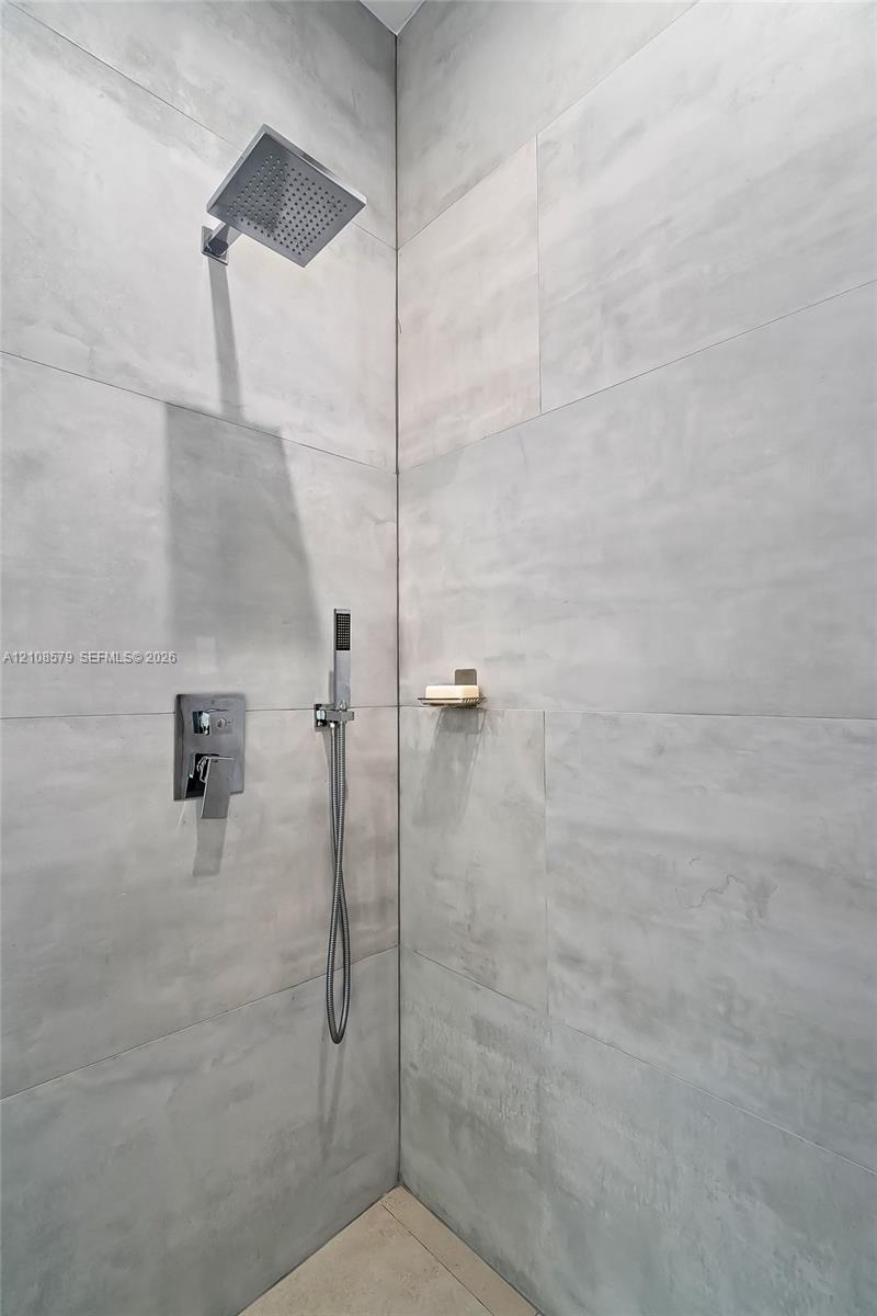 Walk-in shower featuring large-format stone-finish wall tile, a rainfall showerhead, a separate handheld shower sprayer, and a built-in recessed shelf