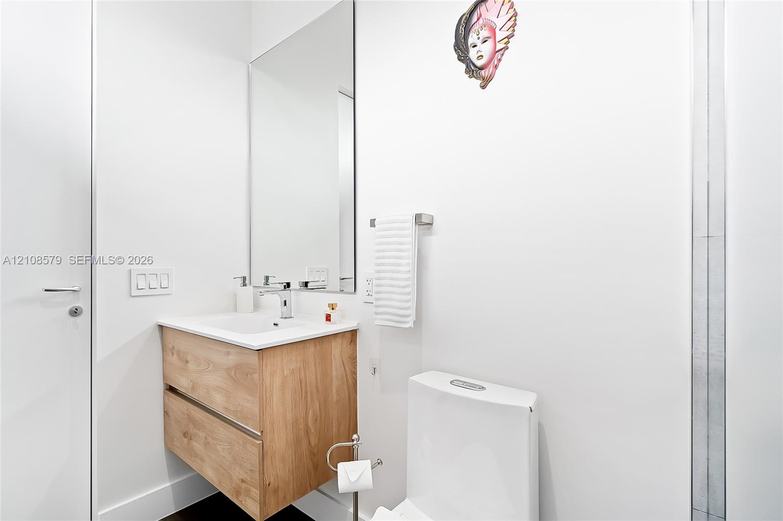 Floating wood-finish vanity with an integrated rectangular sink, wall-mounted polished chrome faucet, and expansive frameless mirror
