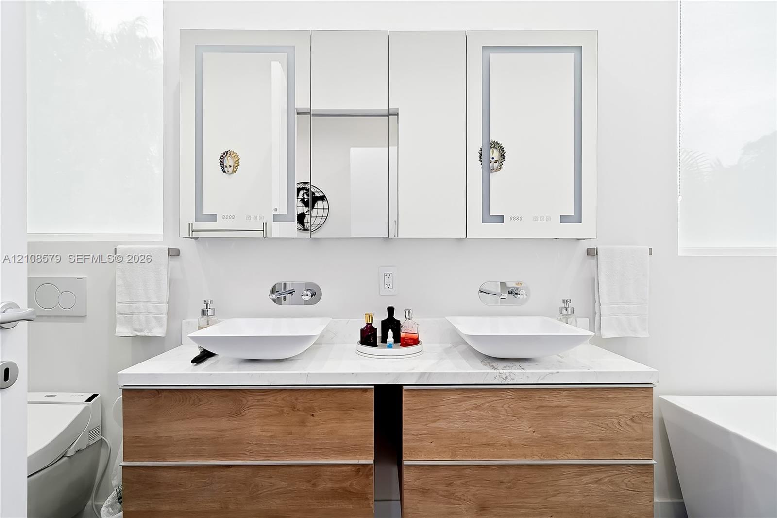 Dual-sink vanity featuring a stone-composite countertop, wood-finish cabinetry, rectangular vessel sinks, wall-mounted faucets, and integrated LED-lit medicine cabinets