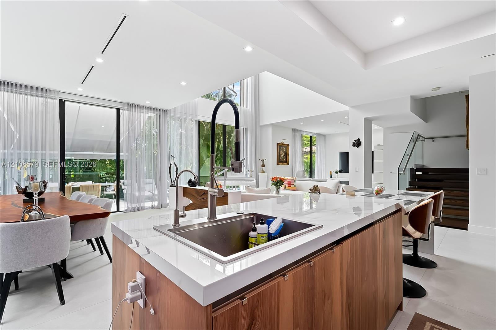 Kitchen island featuring light stone countertops, wood-finish cabinetry, a stainless steel undermount sink, and a high-arch pull-down faucet