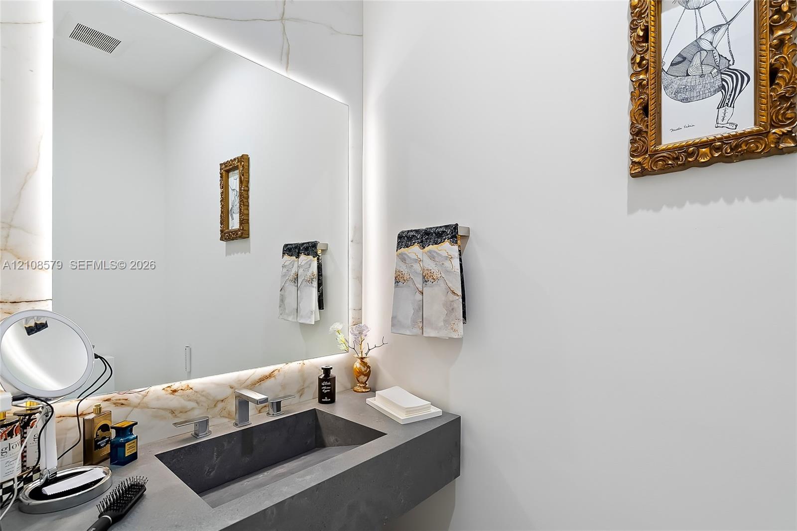 Floating vanity with a charcoal-toned integrated sink, stone-finish backsplash, expansive frameless mirror with integrated LED backlighting, and modern polished metal fixtures