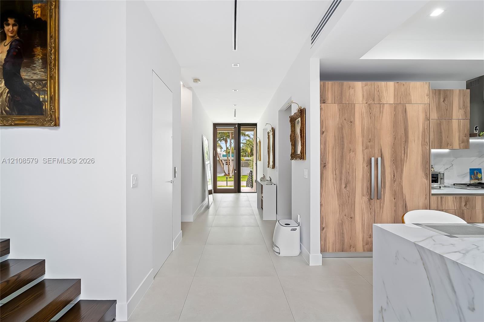 Large-format porcelain tile flooring, wood-finish cabinetry, stone-surface kitchen island with waterfall edge, and custom recessed linear lighting