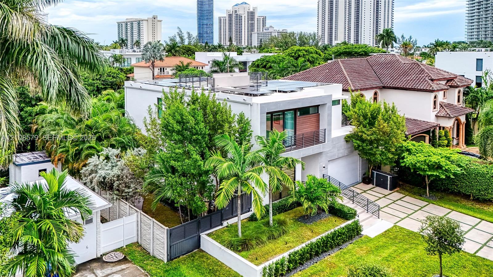 Modern two-story exterior featuring a clean-lined stucco facade, expansive glass balcony, wood-paneled accents, integrated solar panels, and a paved grid driveway