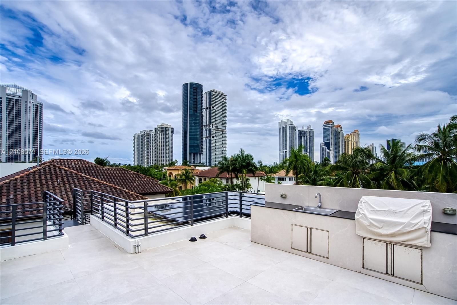 Rooftop terrace featuring large-format tile flooring, metal railings, and a built-in outdoor kitchen with a stainless steel sink and stone countertop