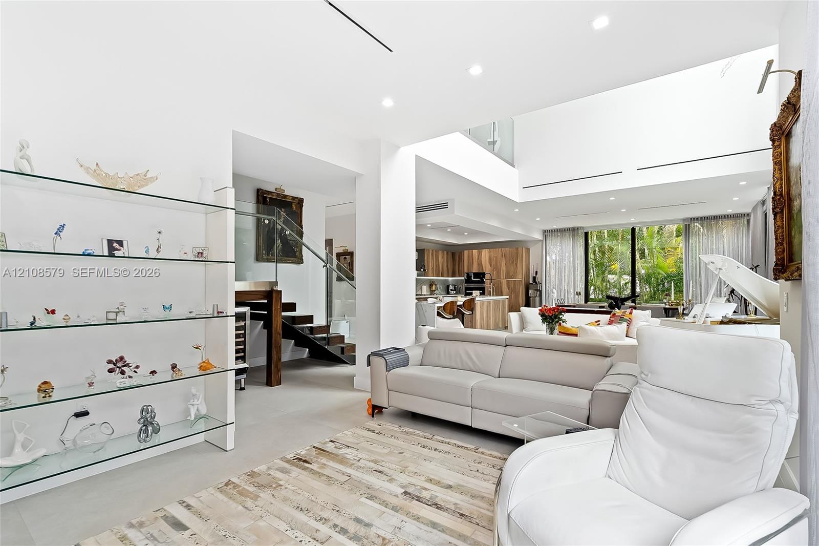 Open-concept floor plan featuring high ceilings, recessed lighting, built-in glass shelving, a glass-paneled staircase, and large-format tile flooring