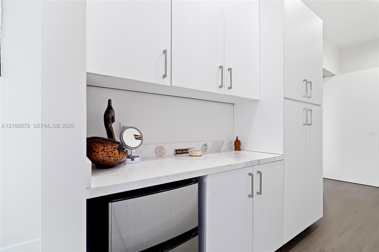 Custom cabinetry with white finish, integrated stone-surface countertop, matte metal hardware, and wood-finish flooring