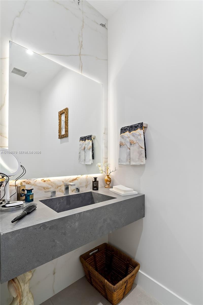 Floating stone vanity with an integrated basin, polished chrome faucet, floor-to-ceiling stone wall cladding, and an expansive mirror with integrated backlighting