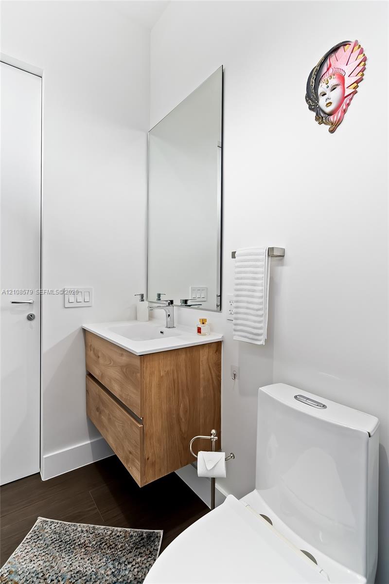 Floating wood-finish vanity with an integrated sink, polished chrome faucet, rectangular wall-mounted mirror, and dark-toned flooring