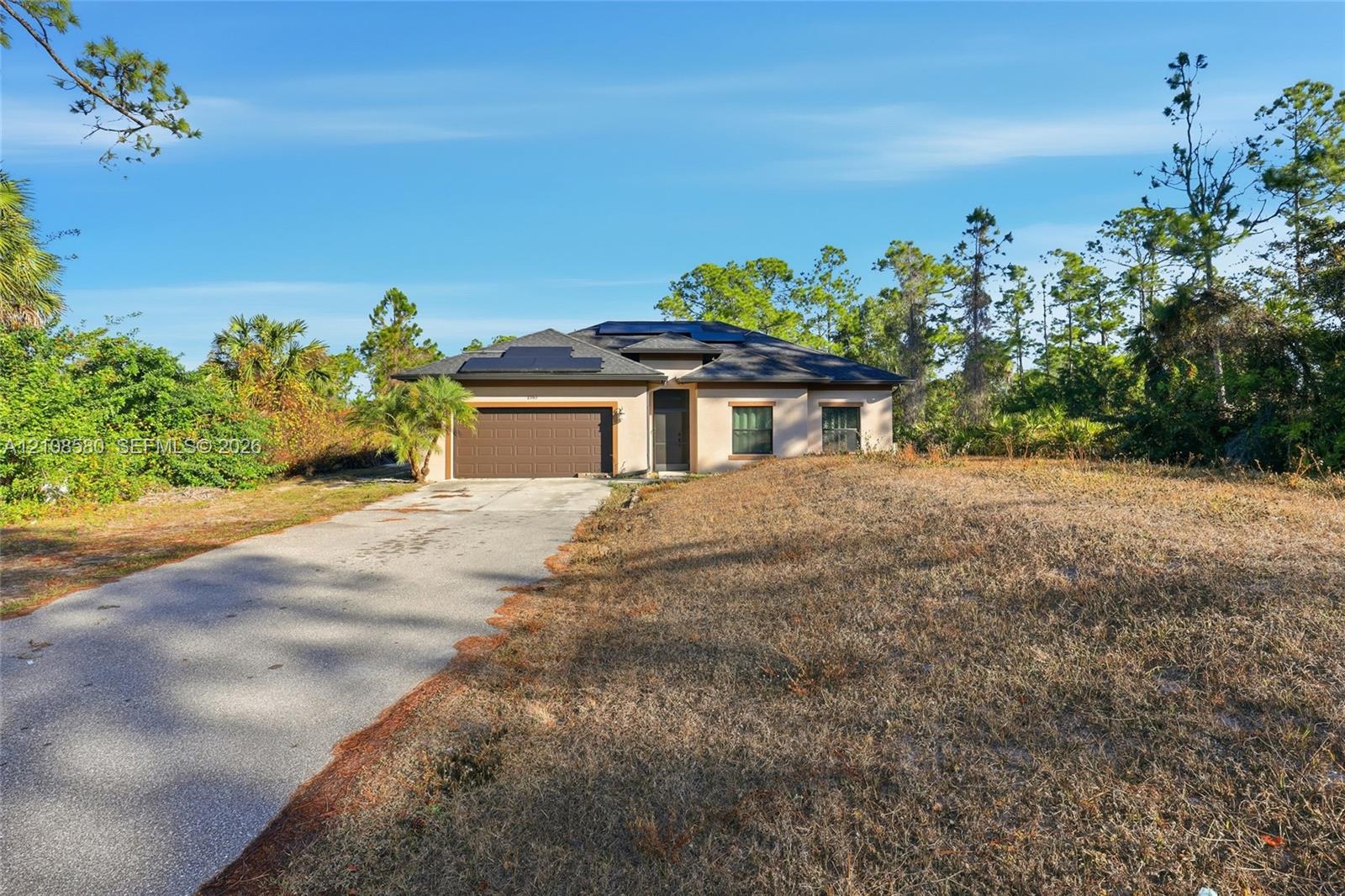 Single-story exterior featuring a concrete driveway, two-car garage, hip roof with installed solar panels, and stucco siding
