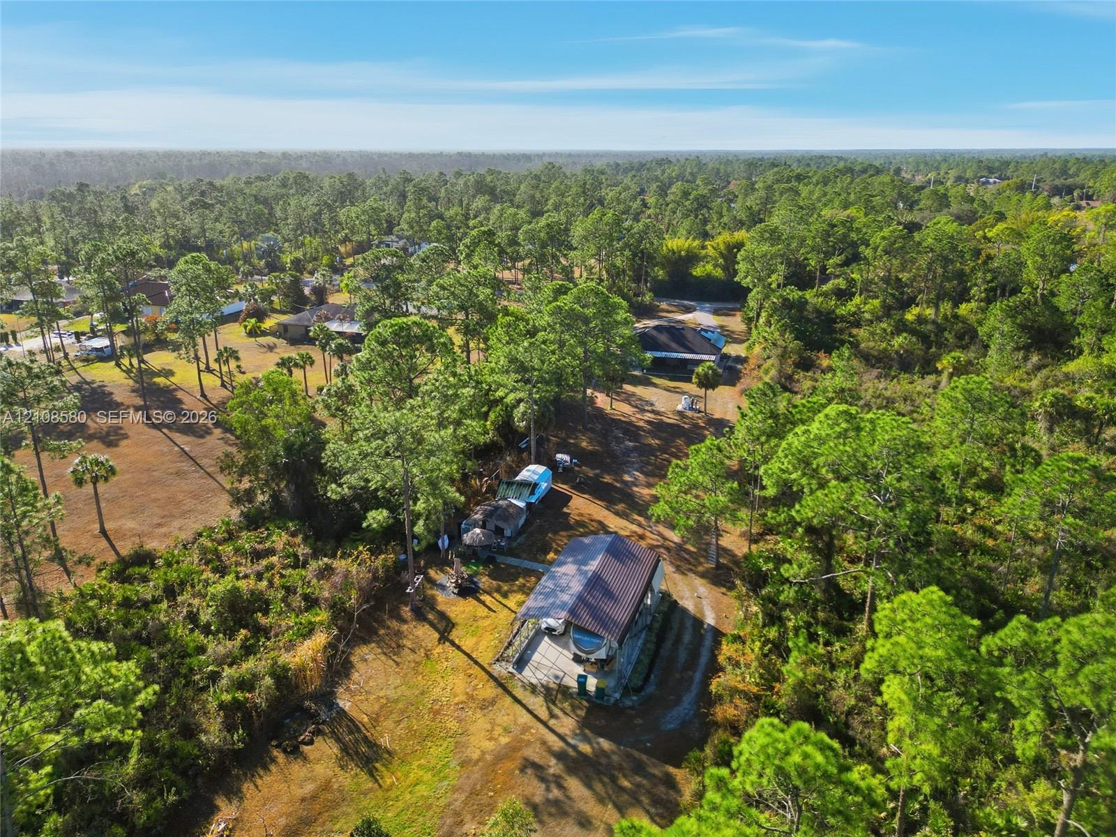 Aerial perspective featuring a metal-roofed structure with an attached carport, situated on a large, wooded parcel with native vegetation