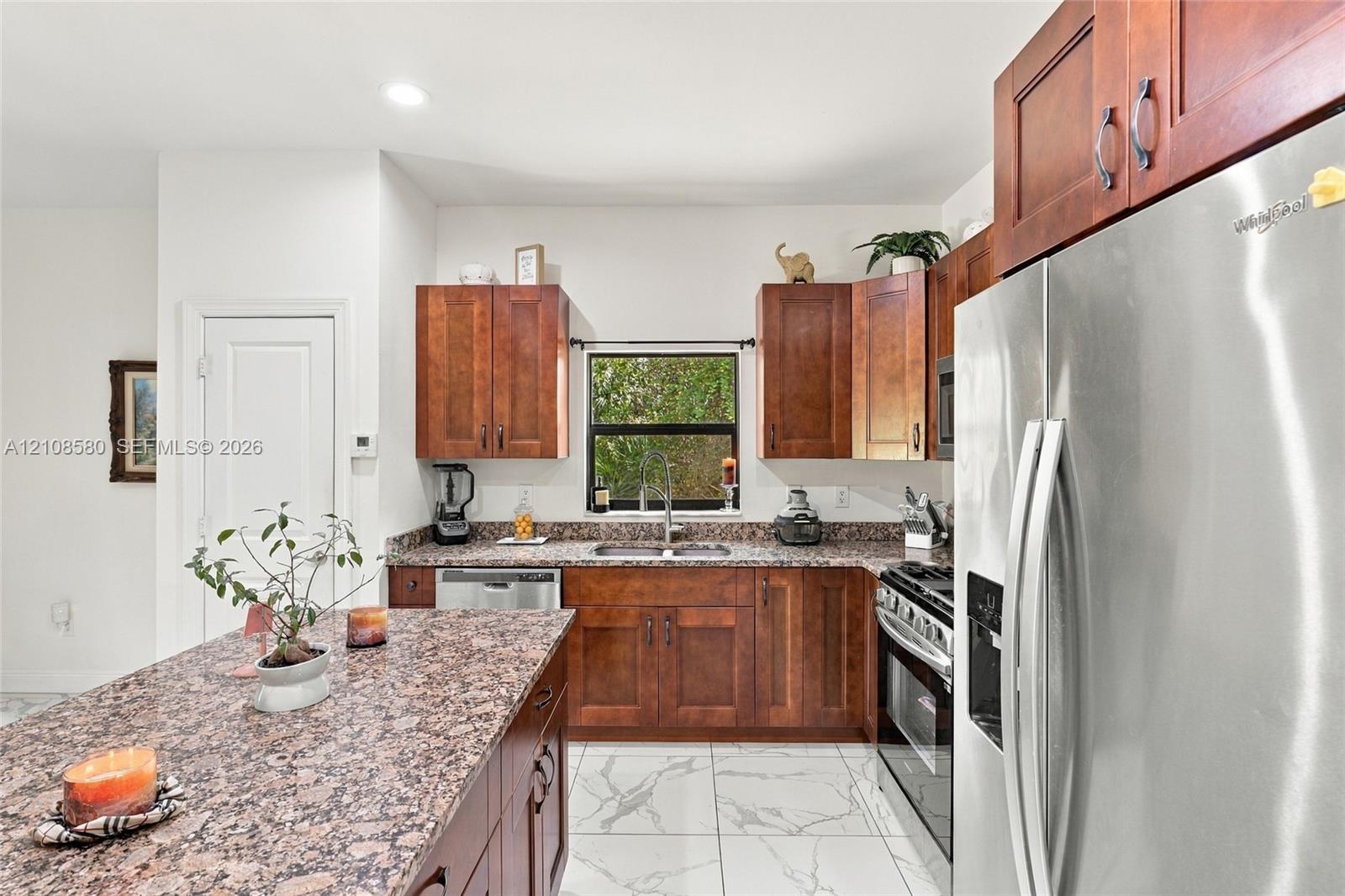 Kitchen featuring wood cabinetry, stone countertops, a central island, stainless steel appliances, and large-format tile flooring