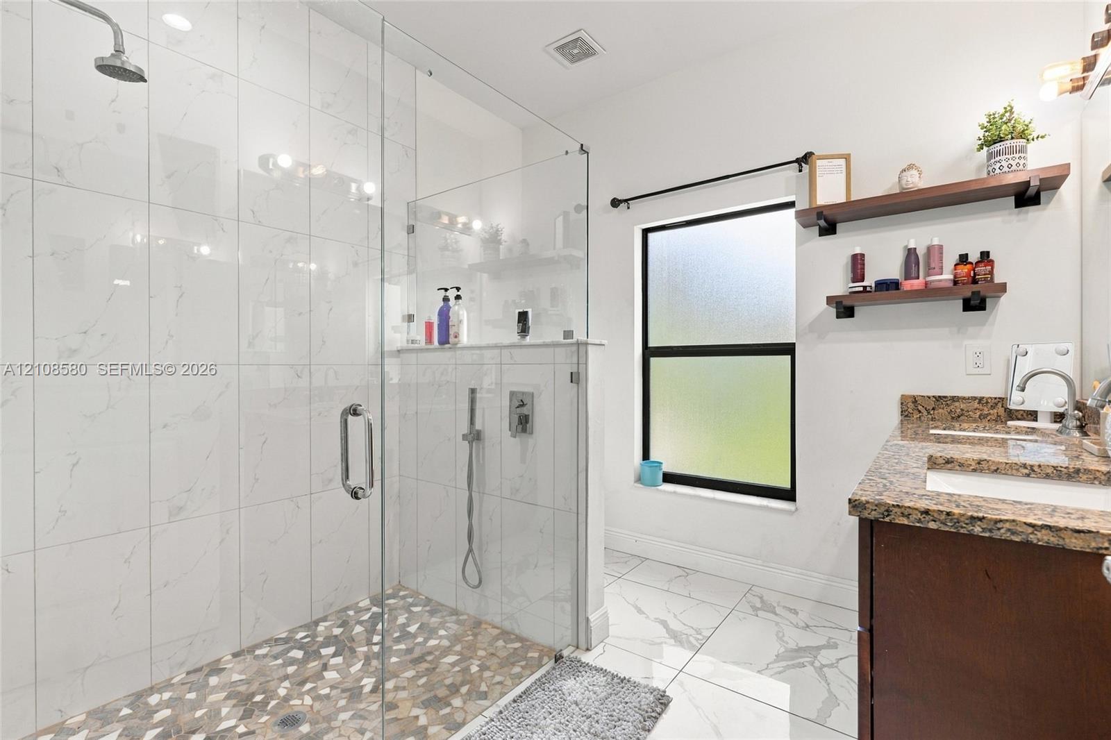 Walk-in shower featuring glass paneling, floor-to-ceiling tile surround, and a pebble-stone floor finish