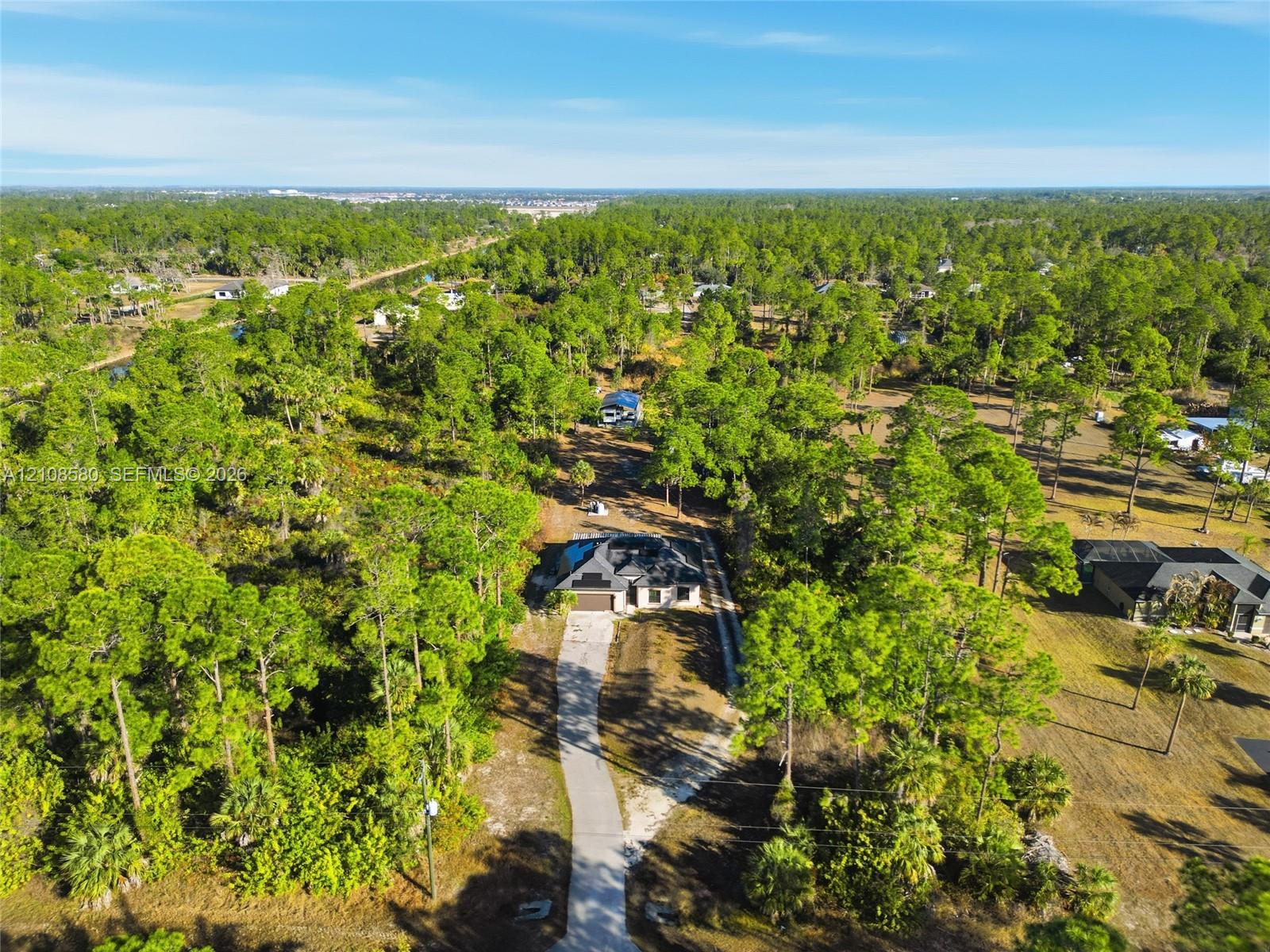 Aerial perspective featuring a single-story residence, a lengthy paved driveway, and extensive surrounding woodland