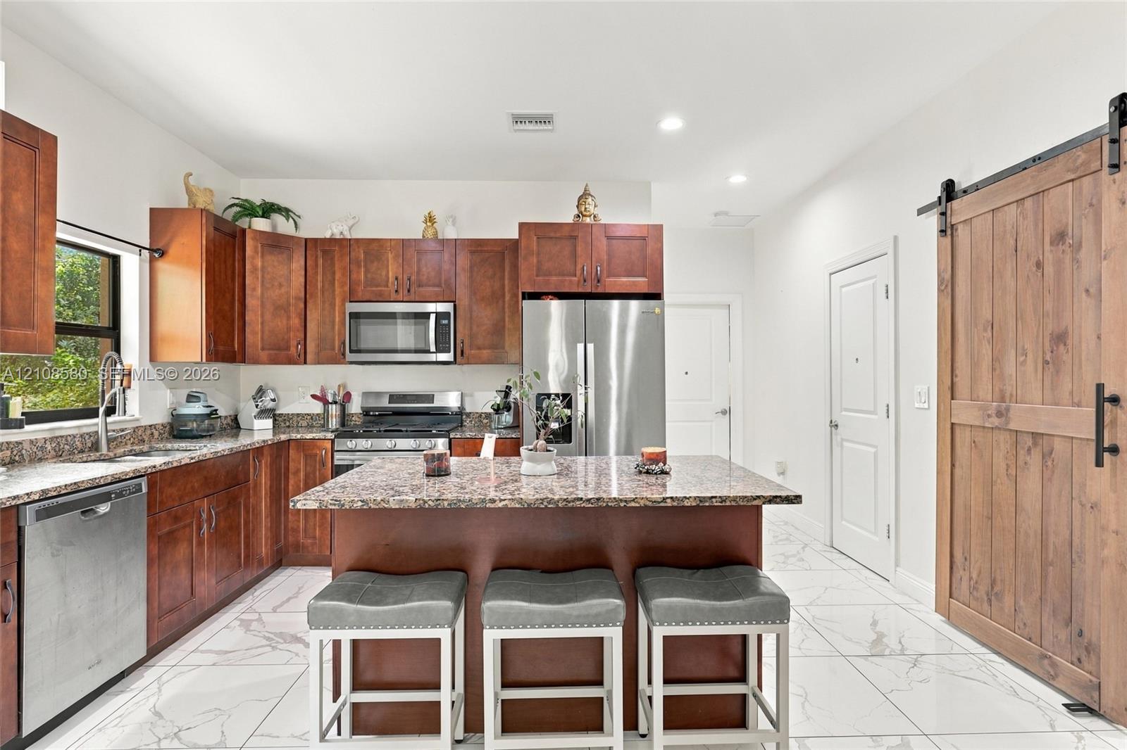 Kitchen featuring wood cabinetry, stone-surface countertops, stainless steel appliances, a central island, and wood-finish sliding barn door