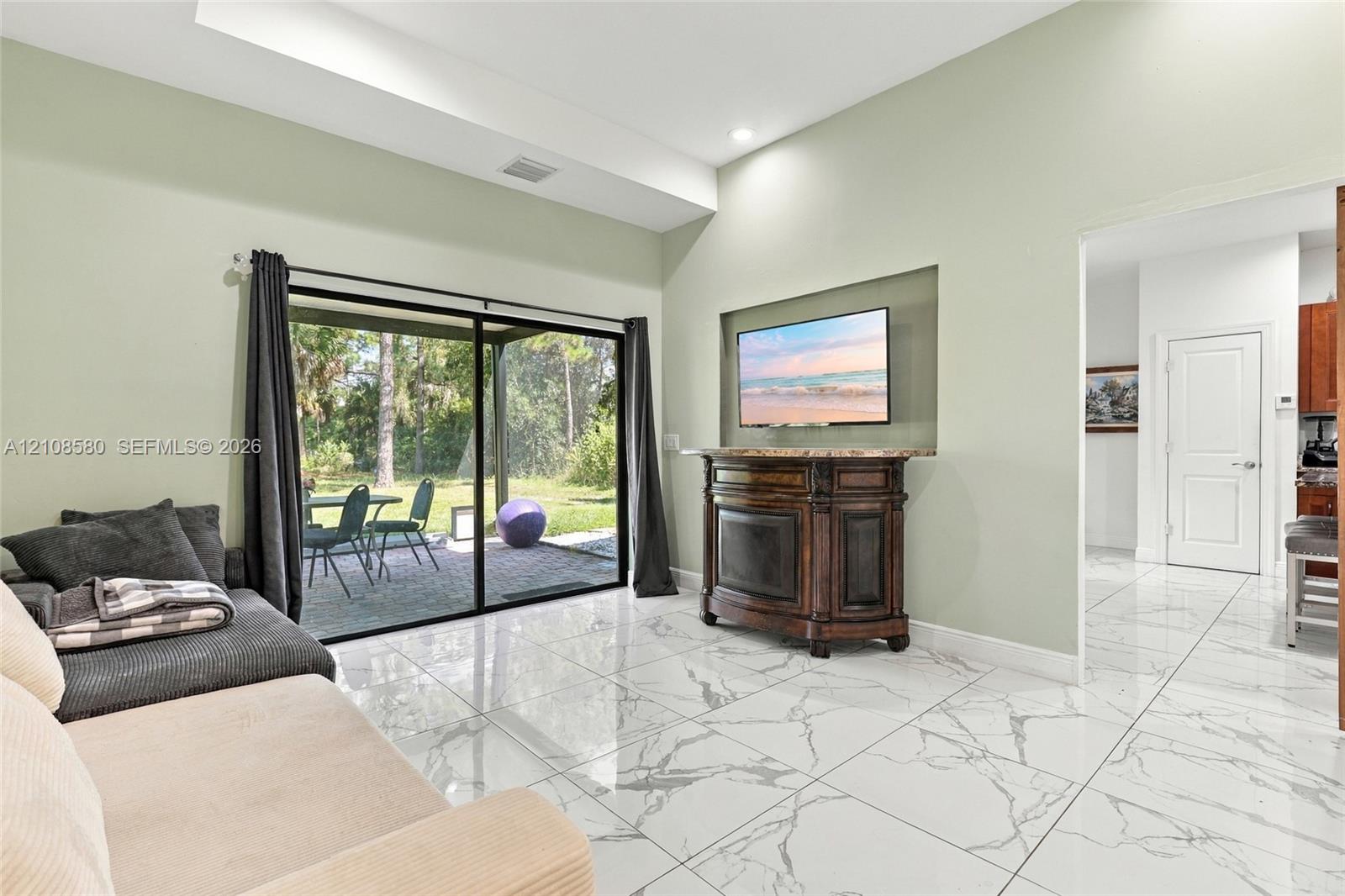 Vaulted ceilings, large-format tile flooring with a marble-style finish, recessed wall niche, and sliding glass doors with access to a paved patio