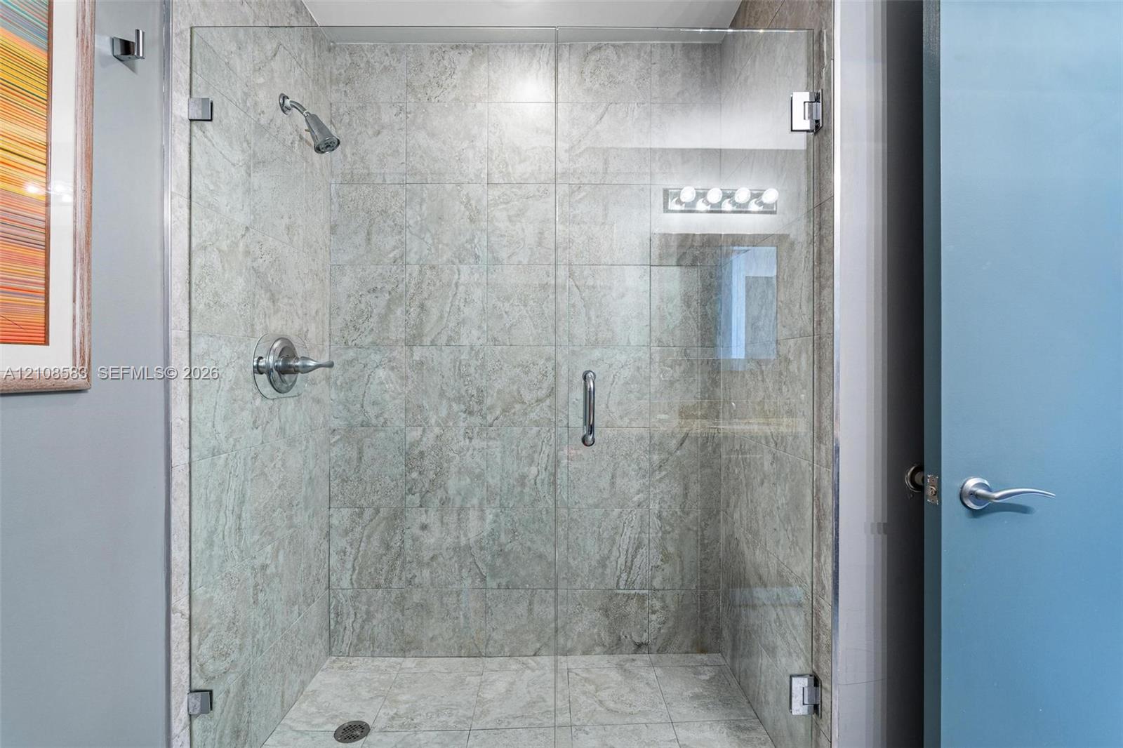 Walk-in shower featuring large-format stone-tile surround, glass enclosure, polished chrome shower head, and matching fixture controls