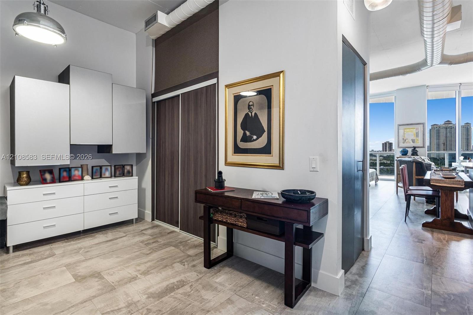 Tile flooring, floor-to-ceiling sliding closet with wood-finish doors, wall-mounted cabinetry with high-gloss finish, and exposed industrial-style ductwork