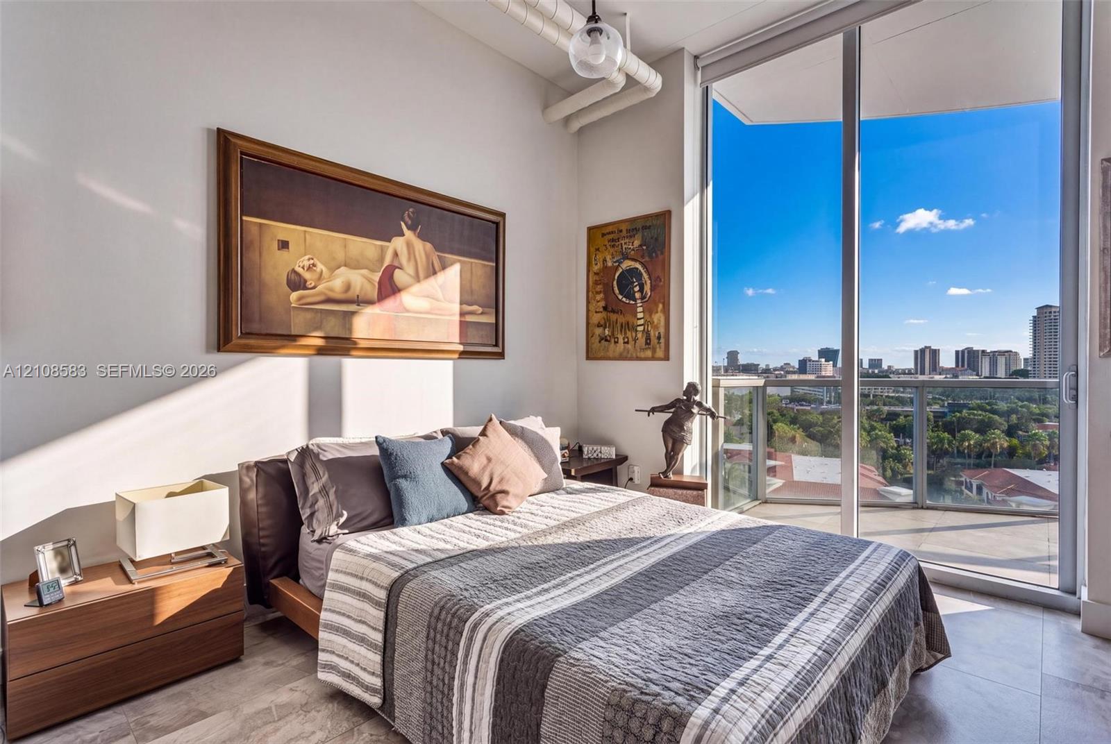 Floor-to-ceiling windows, private balcony, industrial-style exposed ceiling piping, pendant lighting, and neutral stone-finish flooring